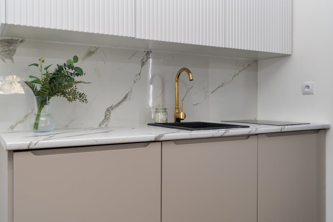 Elegant kitchen interior with marble counters and a gold faucet, featuring greenery for a touch of nature.
